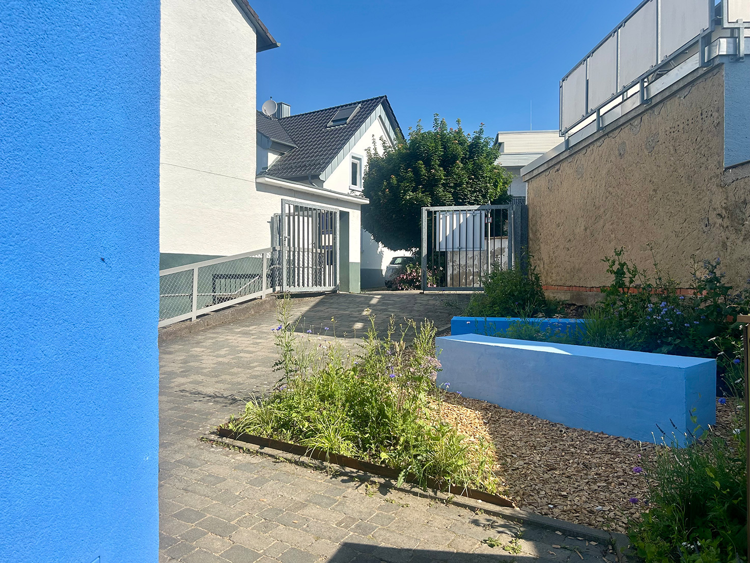 Außenbereich der Kita Sternenwelt mit blauem Sitzblock, Staudenbeeten und Wegen – Projekt HIKITA von Extrathings Landscape Studios.