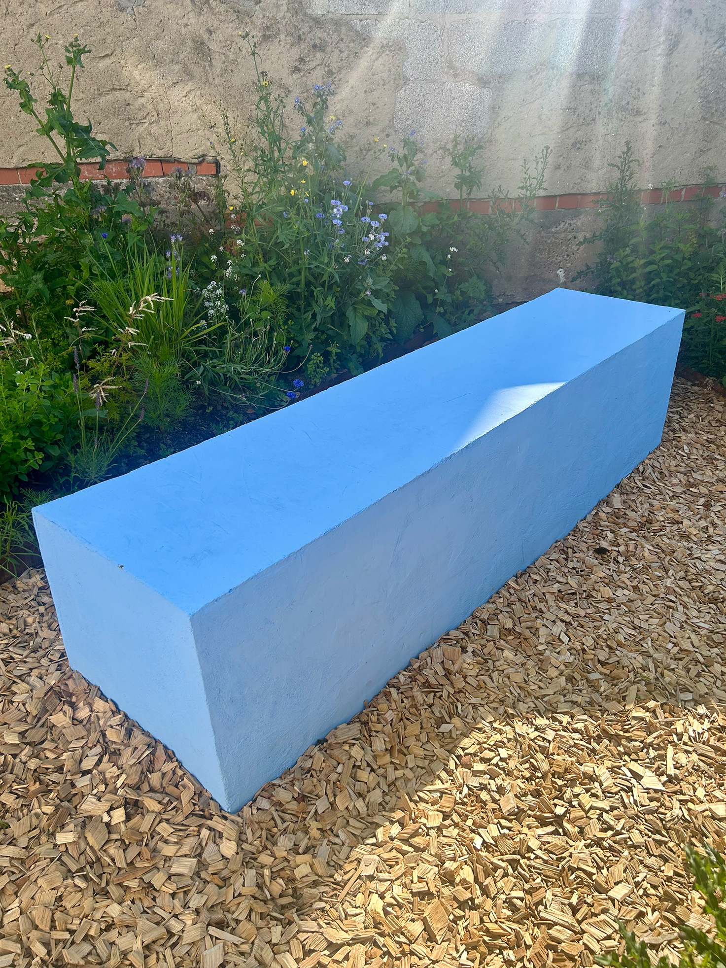 Nahaufnahme eines blauen Betonblocks mit Stauden und Blumen – Freiraum Kita Sternenwelt.