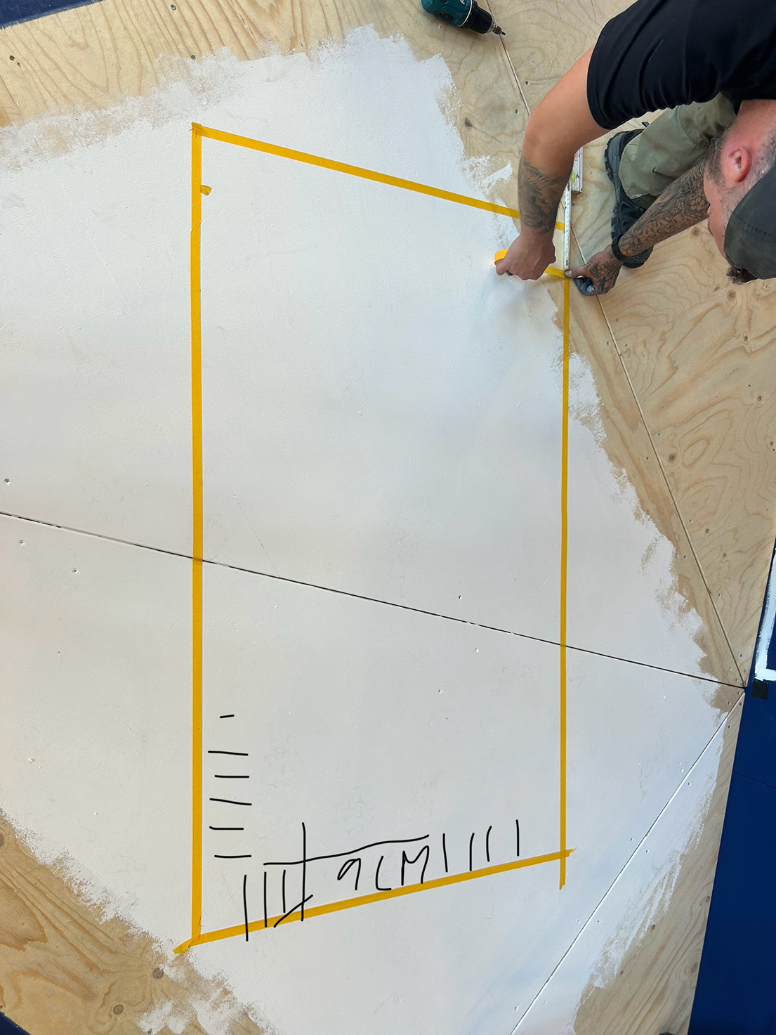 Handwerker markiert mit gelbem Klebeband eine Form auf einer Holzfläche – Bühnenbau für ‚Das doppelte Lottchen.