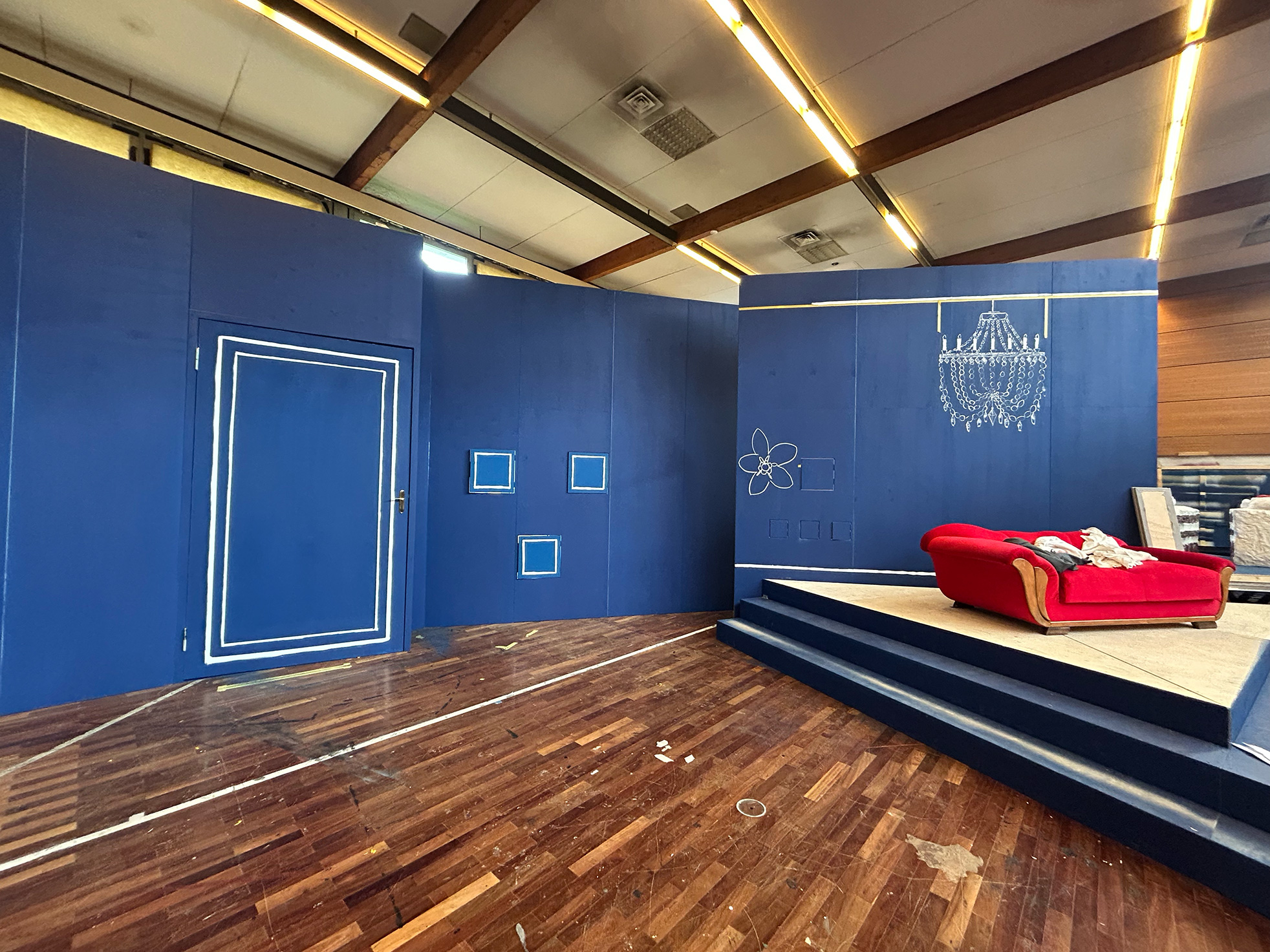 Bühnenbild mit tiefblauen Wänden, weißen Linienzeichnungen und rotem Sofa auf Podest – minimalistisches Setdesign für die Inszenierung ‚Das doppelte Lottchen‘ von Extrathings..