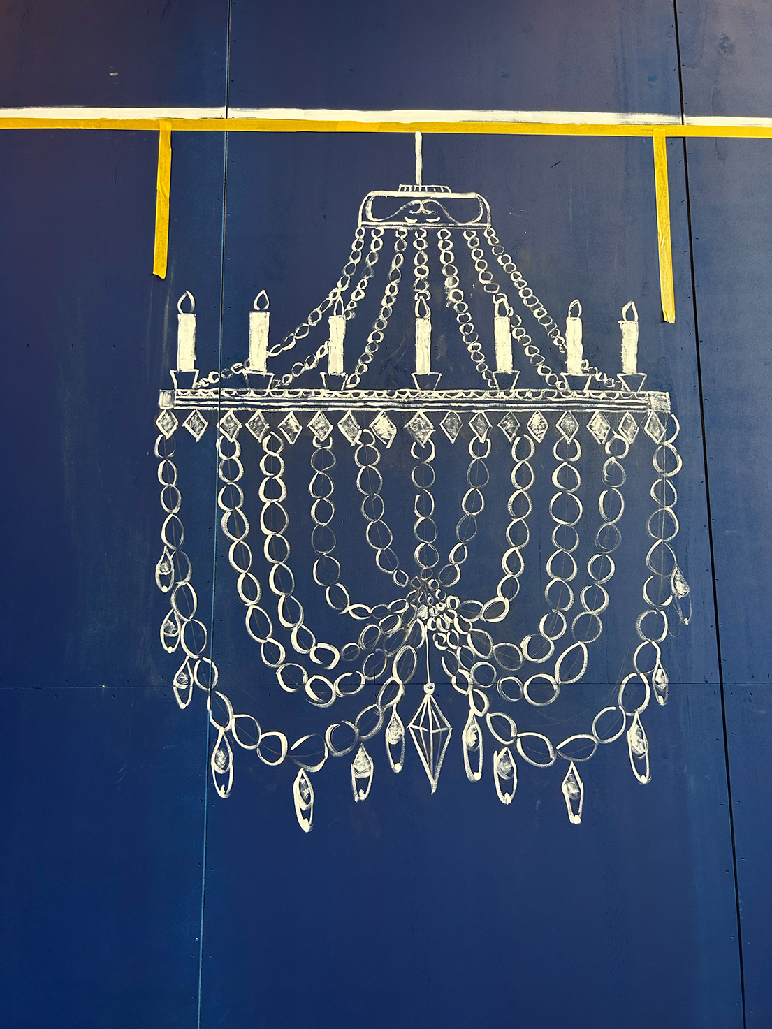 Detailaufnahme einer Wandzeichnung: weiß illustrierter Kronleuchter auf tiefblauer Bühnenwand – minimalistisches Bühnenbild für ‚Das doppelte Lottchen‘ von Extrathings.